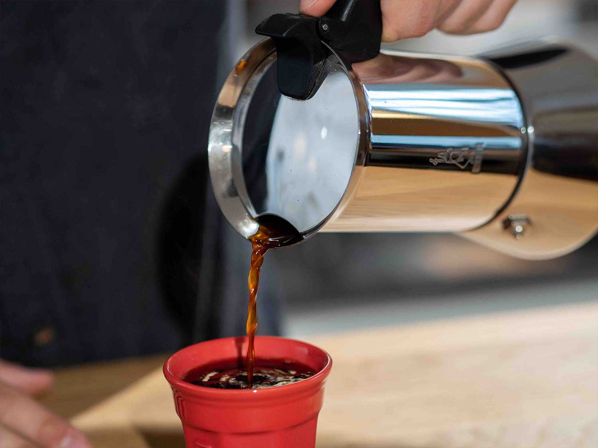 Espresso läuft aus einer Mokkakanne in eine kleine rote Tasse